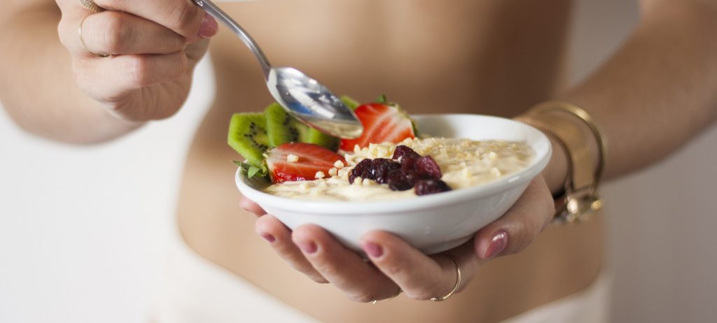 Manos de mujer comiendo un bol de cereales y frutas.