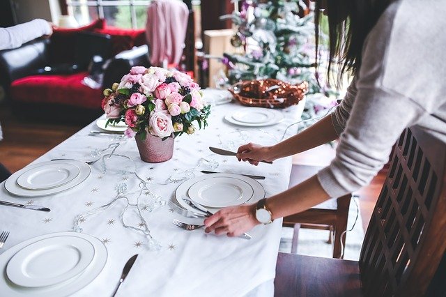 Mujer preparando la mesa para la alimentación de su familia, con unas flores rosas en el centro.