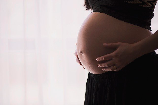 Barriga de mujer embarazada con sus manos sobre ella en una habitación con poca luz.