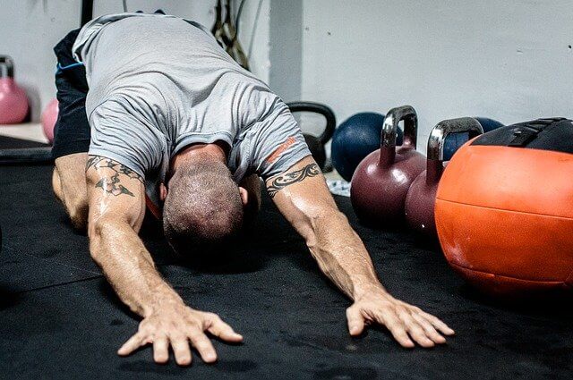 Hombre realizando ejercicios de estiramiento en el suelo de un gimnasio.
