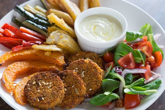 plato lleno de comida vegana como hamburguesas, ensalada, verduras al horno salsa blanca.